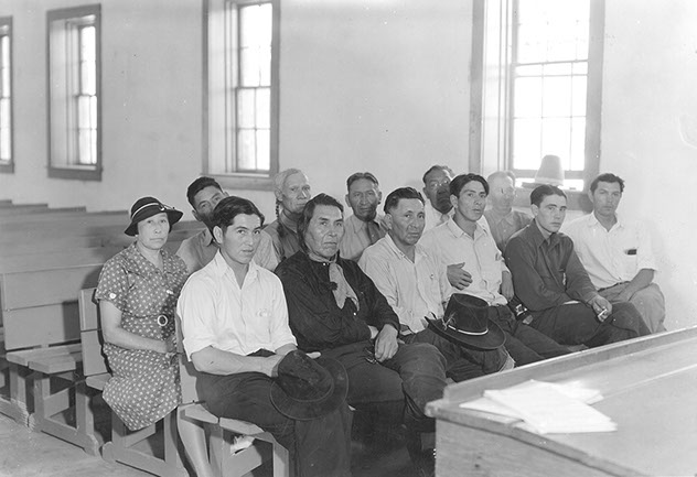 two rows of people sitting in benches, a single woman is sitting at the end of the second row